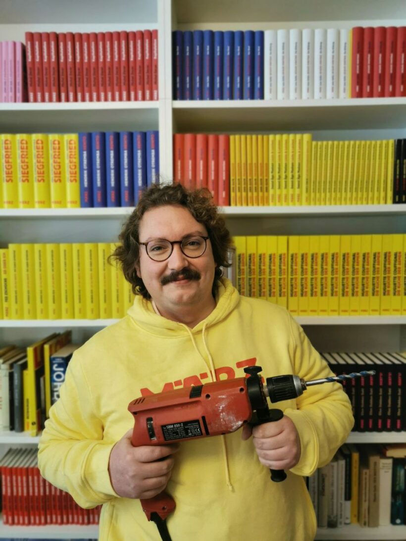 Richard Stoiber mit Bohrmaschine vor Bücherregal
